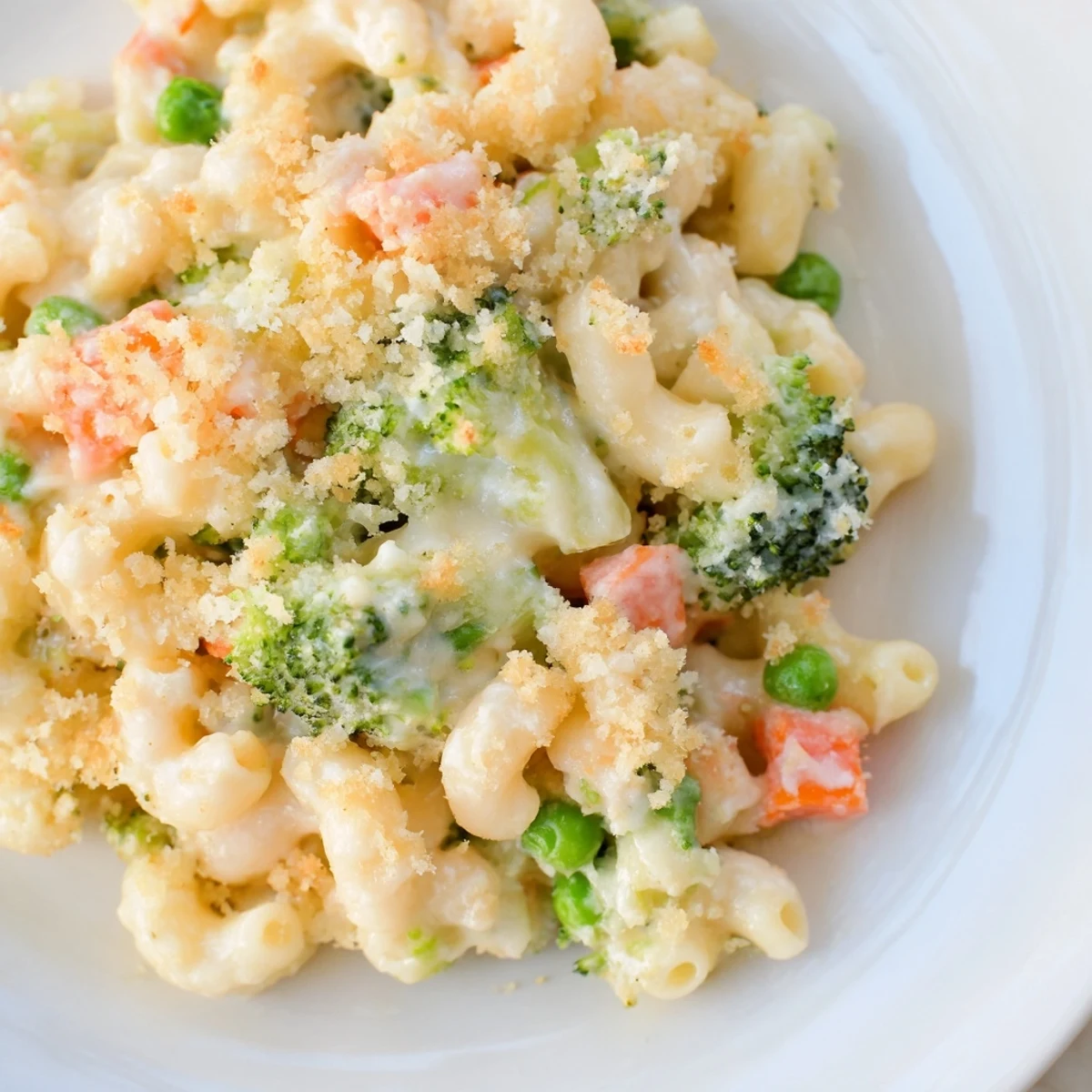 Steaming Garden Veg Mac and Cheese from a golden baking dish, featuring peas, broccoli, and carrots nestled in creamy cheddar sauce with a crunchy panko topping.