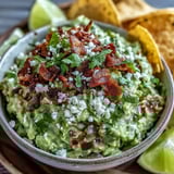 A close-up shows guacamole with Cotija cheese and bacon bits beside blue corn tortilla chips and a cold Mexican lager.