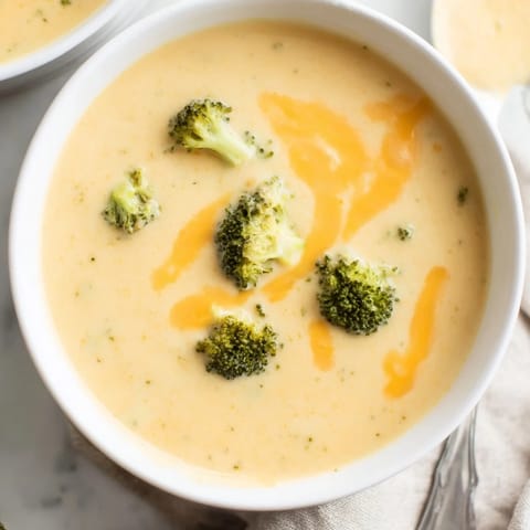 Steaming hot broccoli cheddar soup is ladled into a rustic bread bowl, ready for a cozy, comforting lunch.