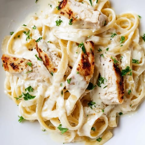 Golden skillet chicken Alfredo over penne pasta in a creamy Parmesan sauce, garnished with fresh parsley and ready to serve.  