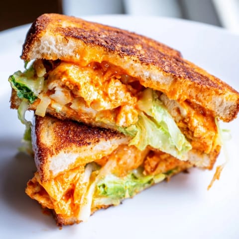 A close-up shows the cheesy, crispy Buffalo Chicken Caesar Grilled Cheese, ready to be enjoyed hot.  