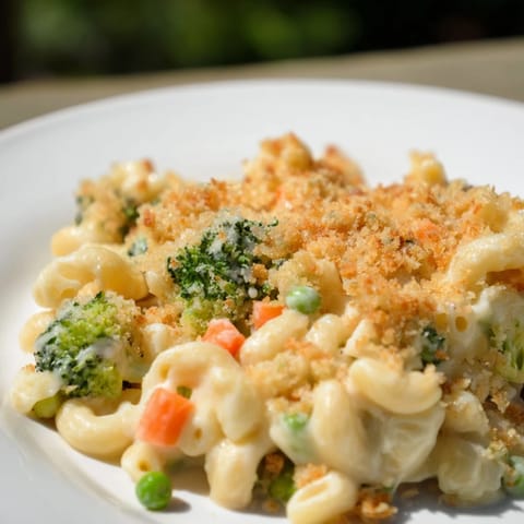 A close-up of homemade Garden Veg Mac and Cheese, showcasing tender broccoli florets, diced carrots, and green peas mingling with velvety, melted cheese sauce.