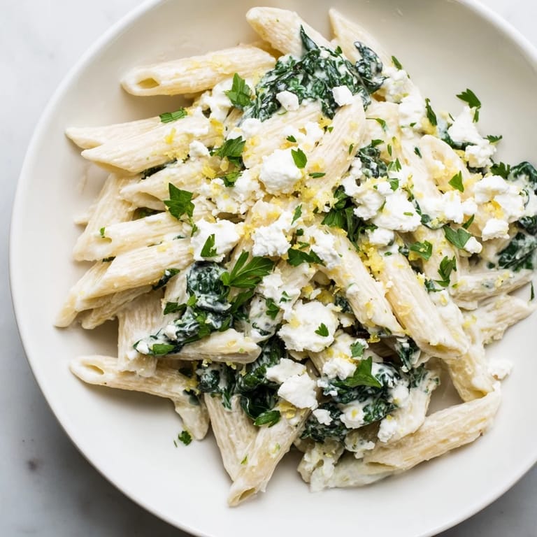 Creamy Feta Spinach Pasta tossed with penne, fresh spinach, and crumbled feta, garnished with lemon zest on a rustic table.