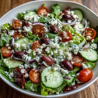 Fresh Mediterranean Green Salad Bowl in a white bowl brims with crisp greens, tomatoes, cucumber, olives, and crumbled feta.